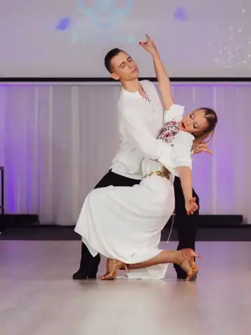 Танцова двойка в сценична поза с бял костюм и рокля.
